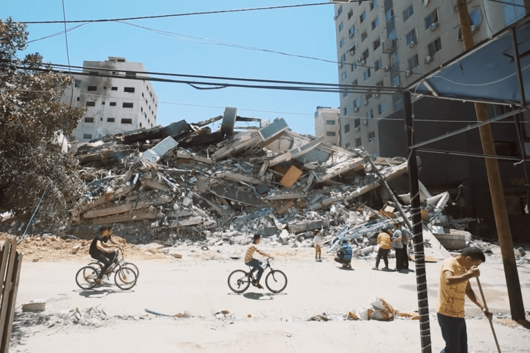 Des jeunes Gazaouis font du vélo devant un bâtiment détruit dans les bombardements sur la bande de Gaza. Mai 2021, Gaza.