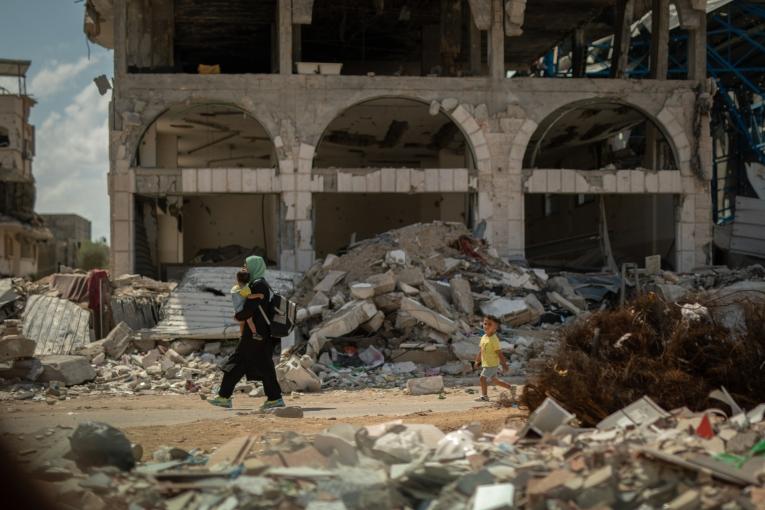 Dans le quartier de Shujaeyya, rue Bagdad, à Gaza, une femme ramène son enfant à la maison à travers les décombres. ©Motassem Abu Aser