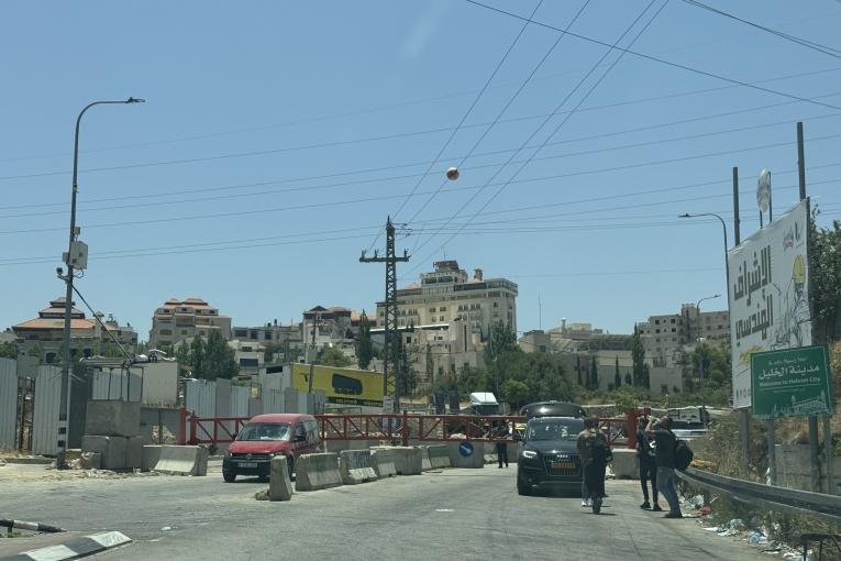 Des personnes attendent devant une barrière israélienne qui bloque l'accès à une route principale menant à Hébron. Beaucoup vont finir par passer à pied, malgré les risques. Ceux qui ont besoin de soins médicaux ou qui ne peuvent pas marcher sont restés bloqués, dans l'impossibilité de traverser. Cisjordanie, 14 juin 2025