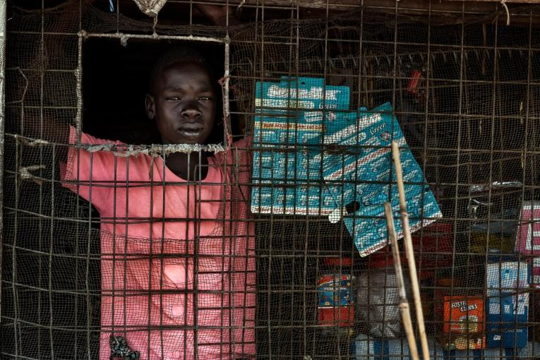 Un jeune garçon gère un petit magasin de denrées alimentaires de base dans l’un des marchés du camp. Soudan du Sud. 2017.