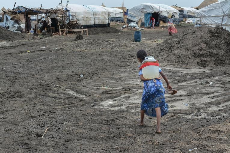 Une jeune fille rapporte un jerrican d'eau dans son abri du camp d'Al Tanideba au Soudan. 2021.