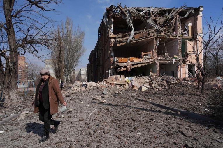 Une femme passe devant un bâtiment endommagé par un bombardement à Marioupol, Ukraine. 13 mars 2022.