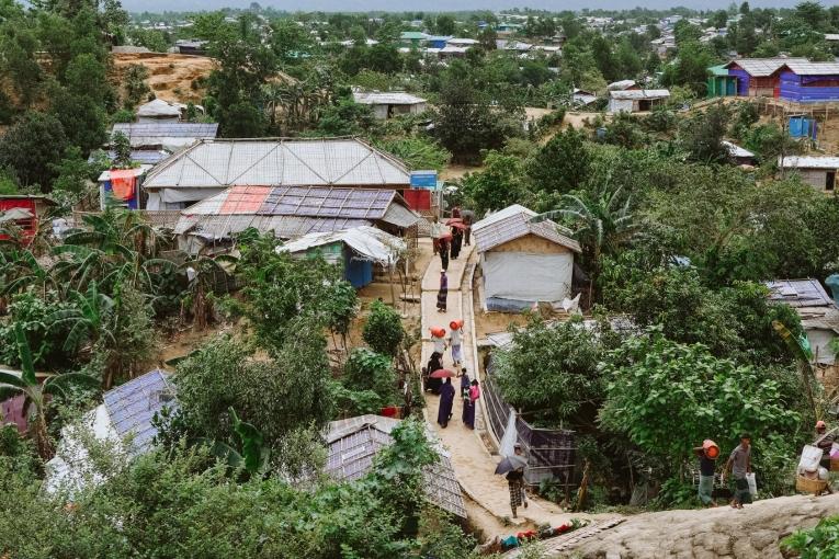 Des réfugiés rohingyas retournent à pied dans un camp, chargés de provisions provenant d'un point de distribution.