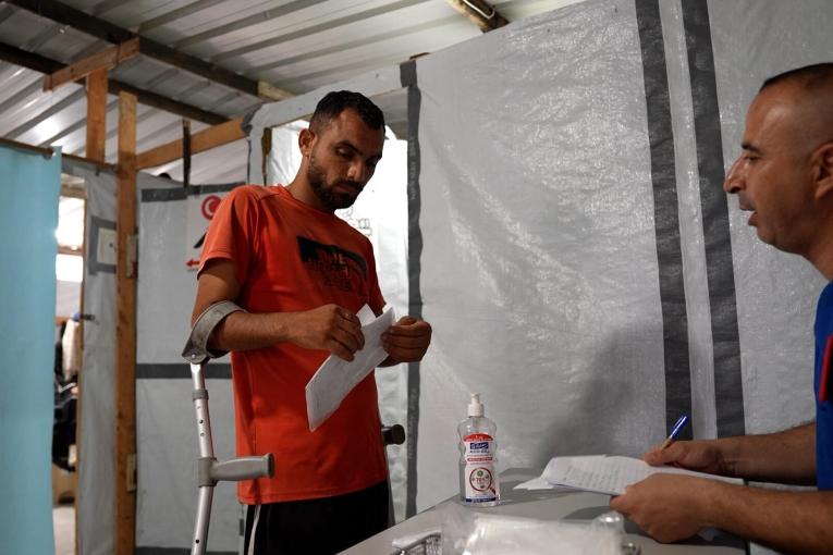 Un membre du personnel de MSF consulte le dossier médical de Saad Hussein, contraint de vivre avec un fixateur externe depuis qu'il a été blessé en 2025 lors d'une distribution alimentaire organisée par la Fondation humanitaire de Gaza. 