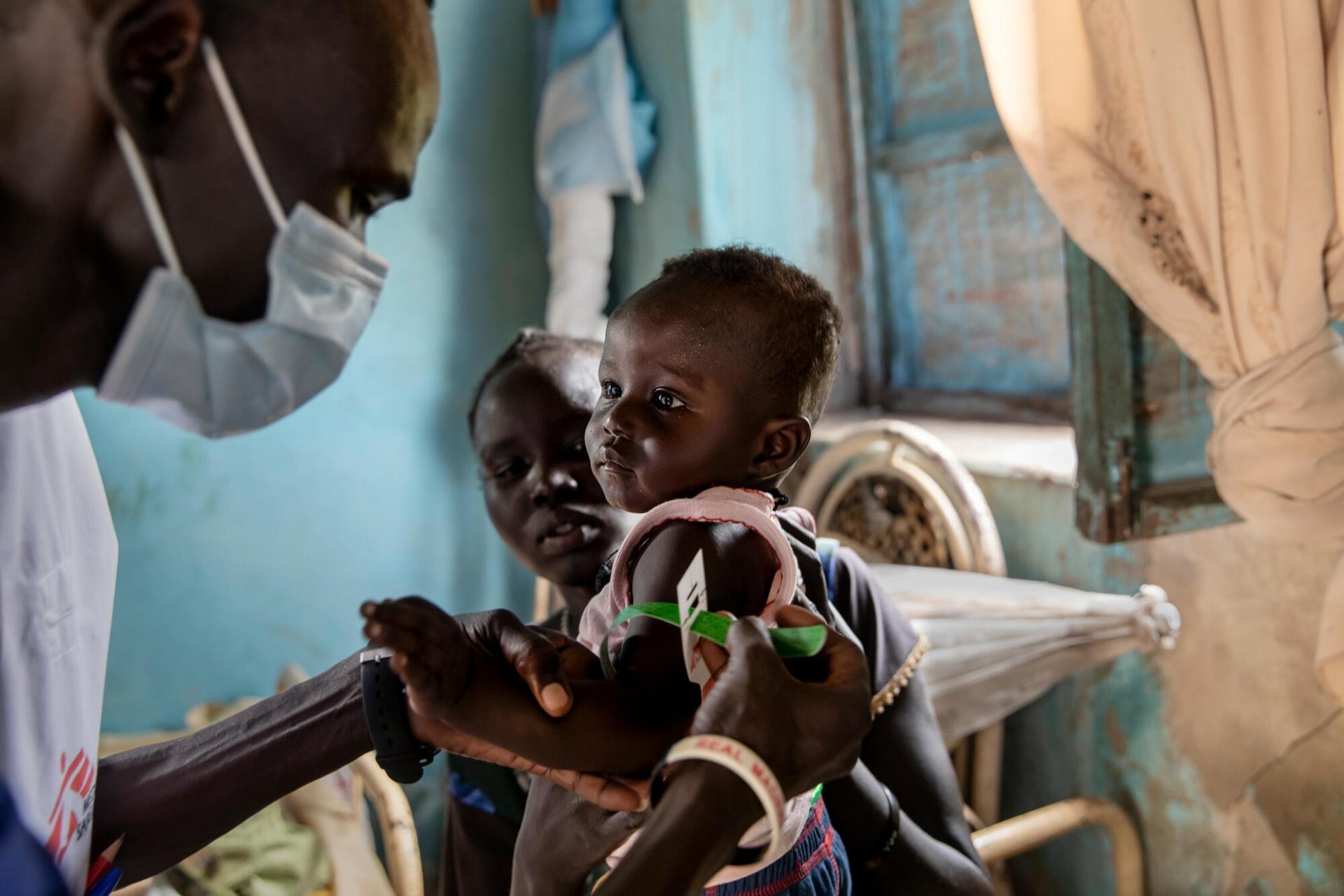 Dans sa maison de Kuom, au Soudan du Sud, Ajok Atak tient son bébé Yel dans les bras tandis qu’un membre de MSF mesure le périmètre brachial de l’enfant.