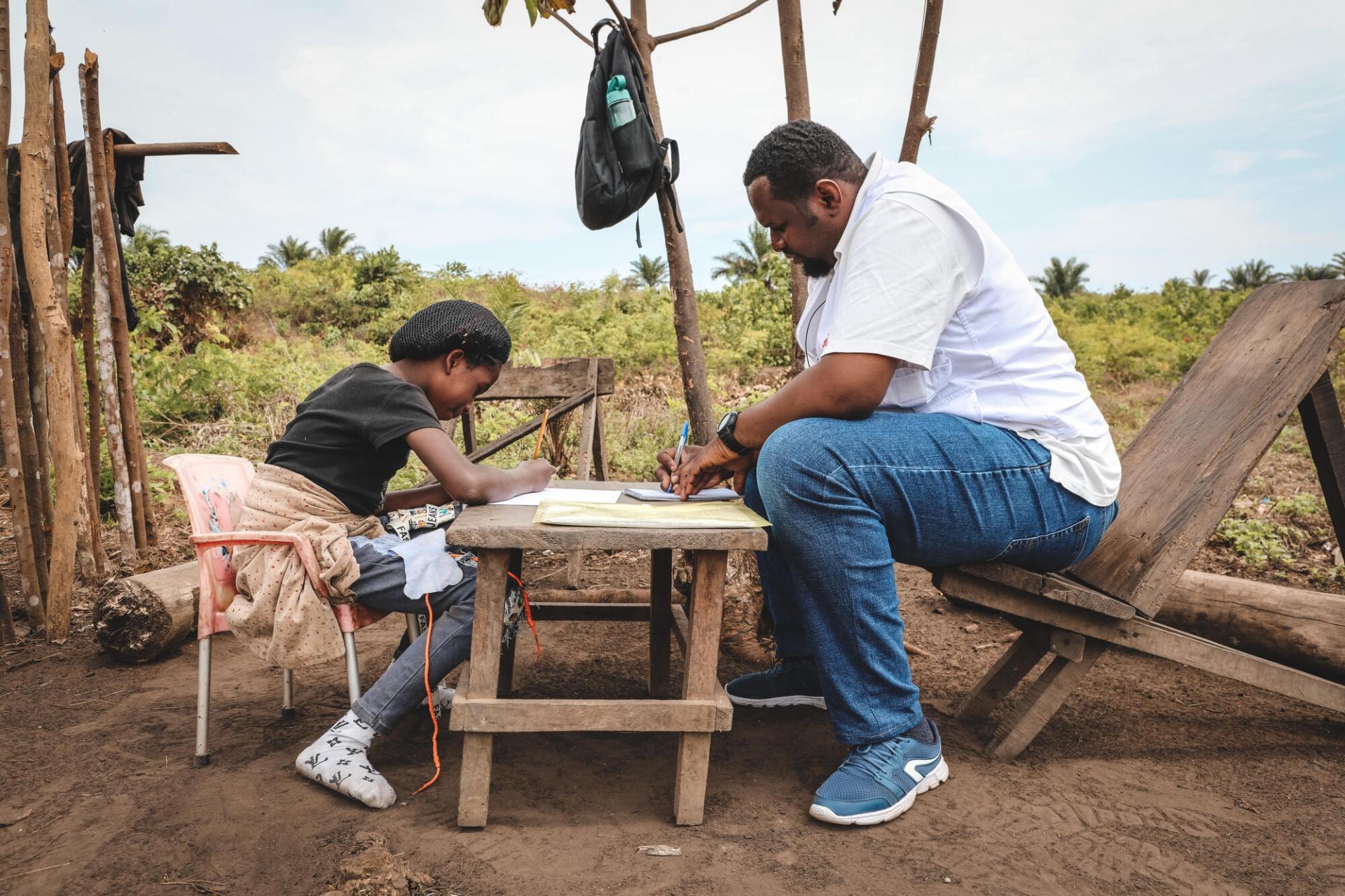 Beverly, 11 ans, et Joel-Christopher Bolombo, psychologue, lors d’une consultation médicale à Kwamouth, en République démocratique du Congo. Les équipes de MSF ont mis en place un soutien en santé mentale dans un camp de personnes déplacées par les violences dans la région. République démocratique du Congo, août 2022