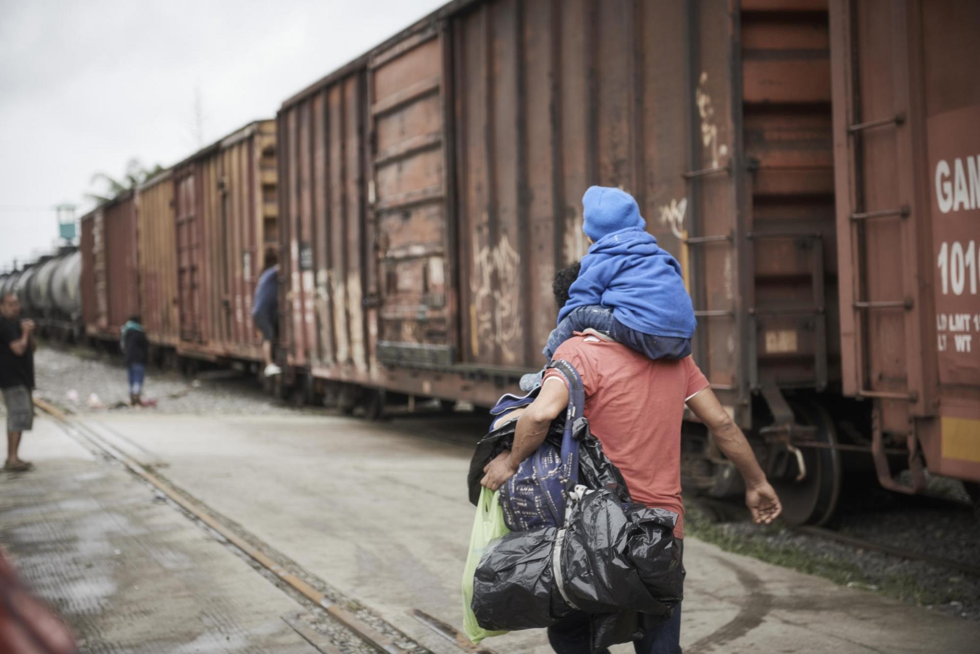 Un homme porte son enfant sur les épaules tandis qu’il cherche à monter dans un train. 