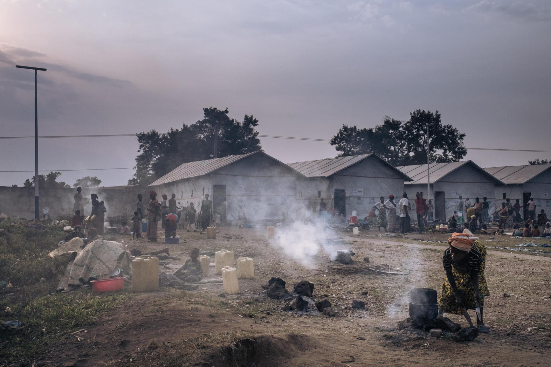 Une femme prépare de la nourriture à l'aube devant les abris communautaires du site informel pour personnes déplacées du stade de Rugabo.