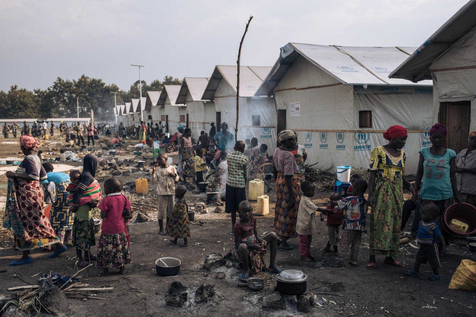 Adultes et enfants préparent à manger devant des abris communautaires sur le site informel de déplacés du stade de Rugabo, dans le centre de Rutshuru.