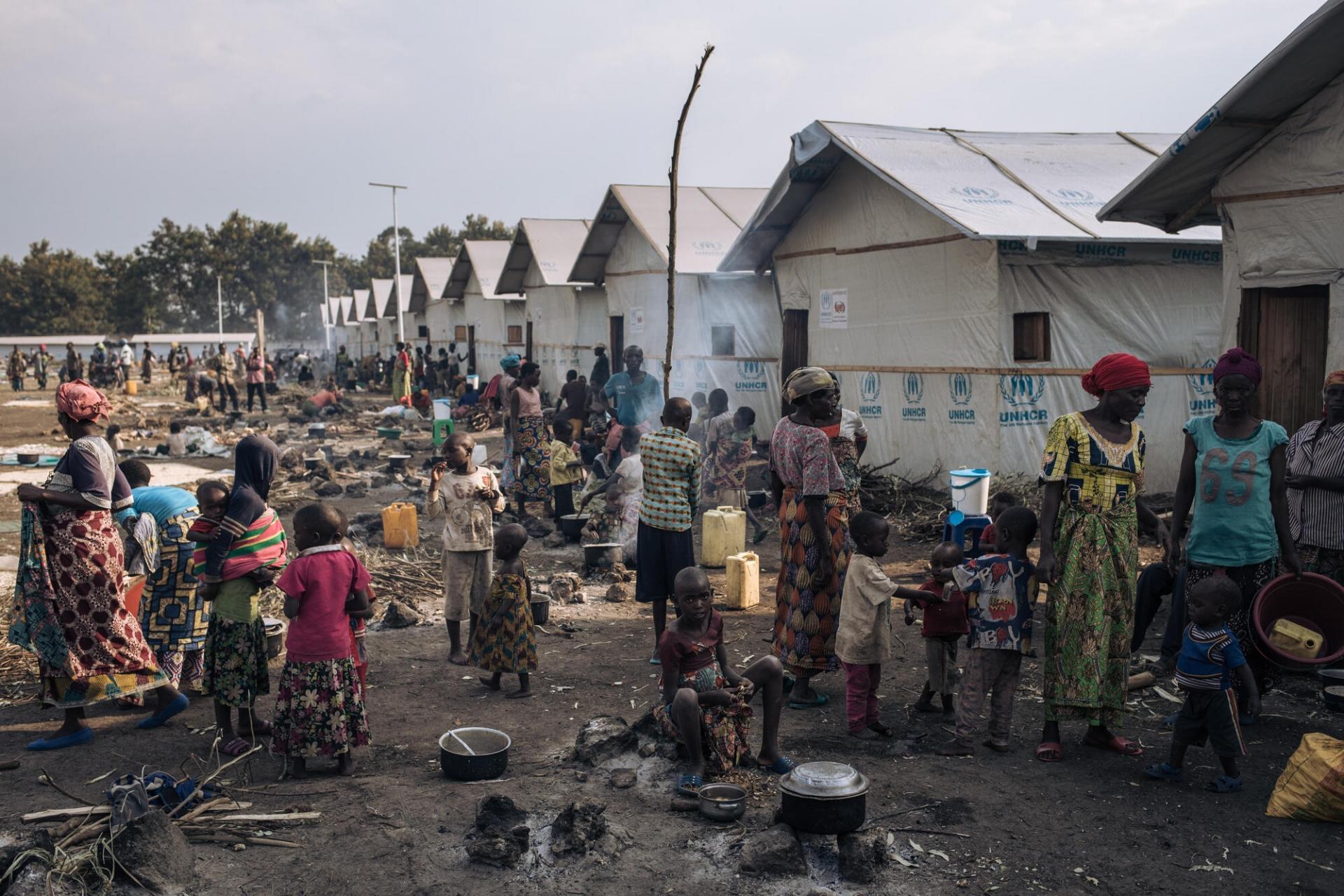 Adultes et enfants préparent à manger devant des abris communautaires sur le site informel de déplacés du stade de Rugabo, dans le centre de Rutshuru.