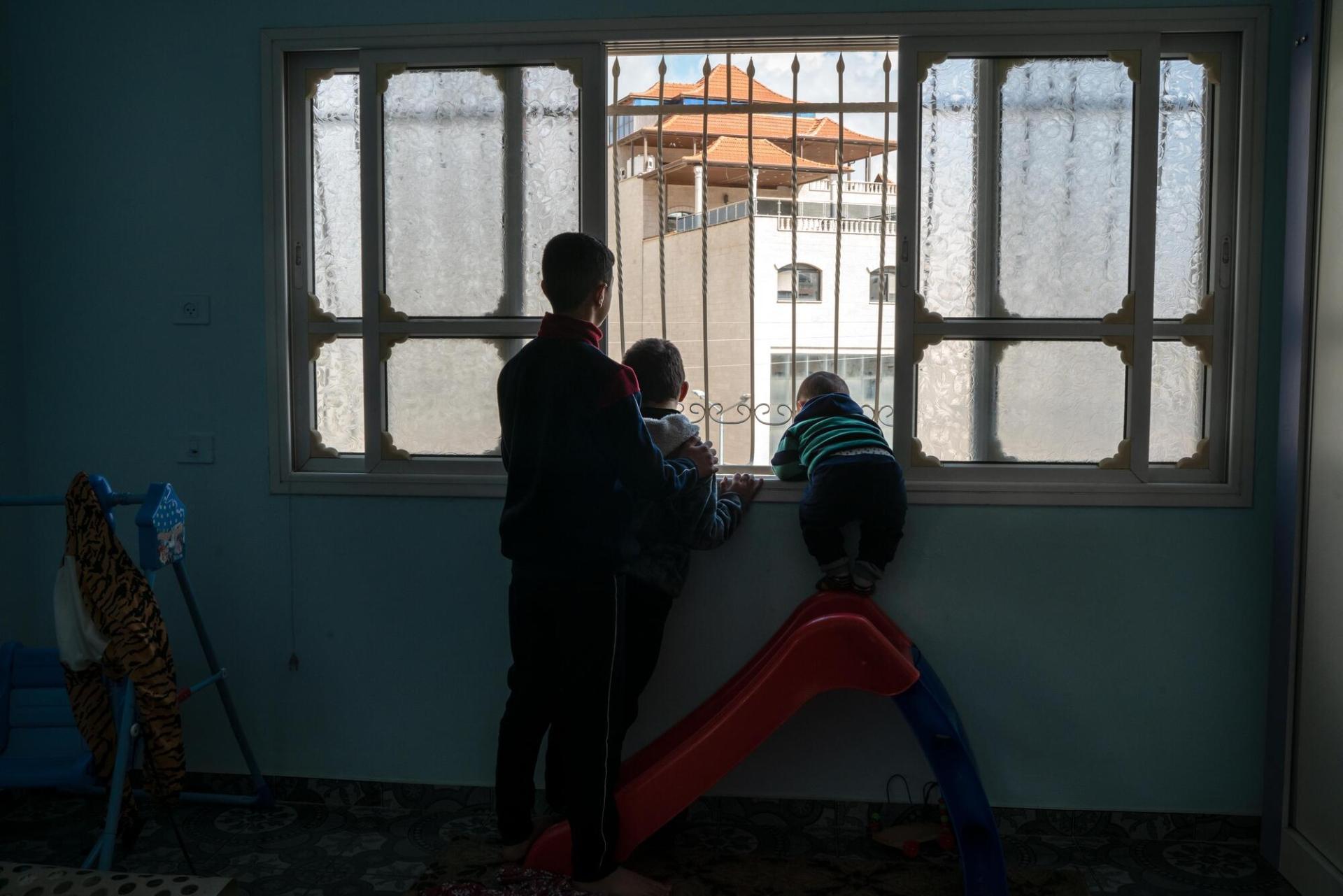 Hussam et ses cousins regardent un soldat israélien par la fenêtre de leur maison de Huwara. Avril 2023. Cisjordanie.