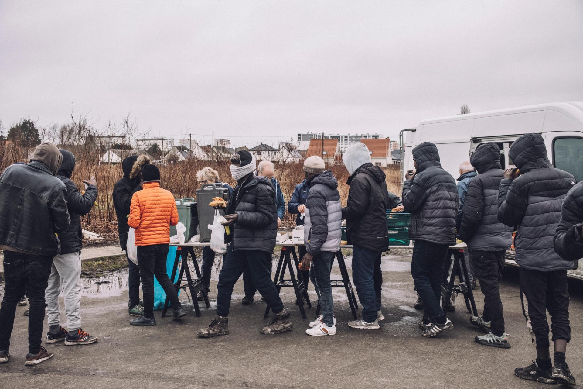 Des migrants font la queue pour recevoir le petit-déjeuner distribué par l’association Salam à proximité d’un petit campement de fortune et de la clinique mobile de MSF, dans le nord de la France, à Calais, le 25 janvier 2024.