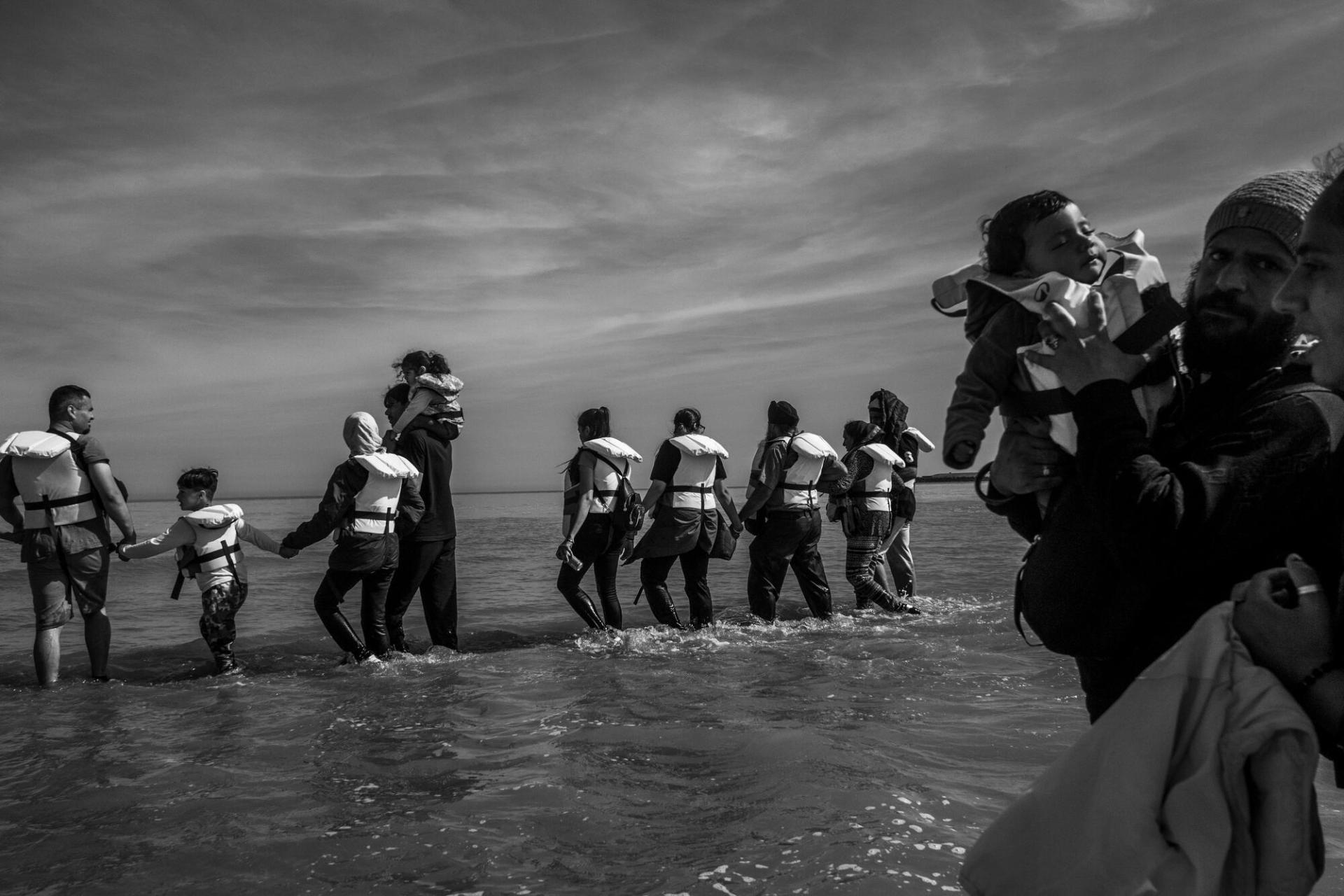 Un groupe d’exilés progresse dans l’eau pour rejoindre un bateau pneumatique, dans le but de traverser la Manche, à Grand-Fort-Philippe, en France.