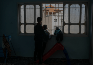 Hussam et ses cousins regardent un soldat israélien par la fenêtre de leur maison de Huwara. Avril 2023. Cisjordanie.