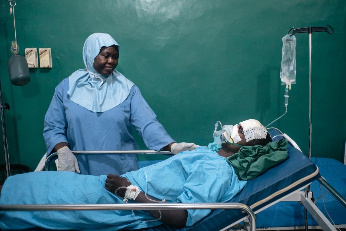 Bilya, 20 ans, un patient atteint de noma, se repose dans la salle de réveil de l'hôpital de Sokoto, après sa première intervention chirurgicale. Lady Bello, infirmière, prend soin de lui. Le personnel s'assure que les patients se rétablissent rapidement et évitent les infections. Quatre fois par an, une équipe de chirurgiens plastiques et maxillo-faciaux, d'anesthésistes et d'infirmières vient à l'hôpital de Sokoto.
 © Claire Jeantet - Fabrice Caterini/Inediz