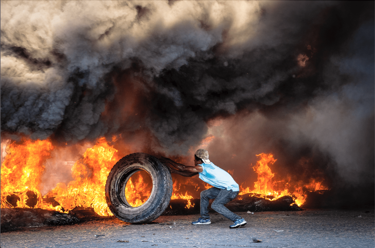 Un manifestant attise un feu de pneus pour bloquer la circulation dans les rues de Port-au-Prince. Mars 2019.
 © Johnson Sabin