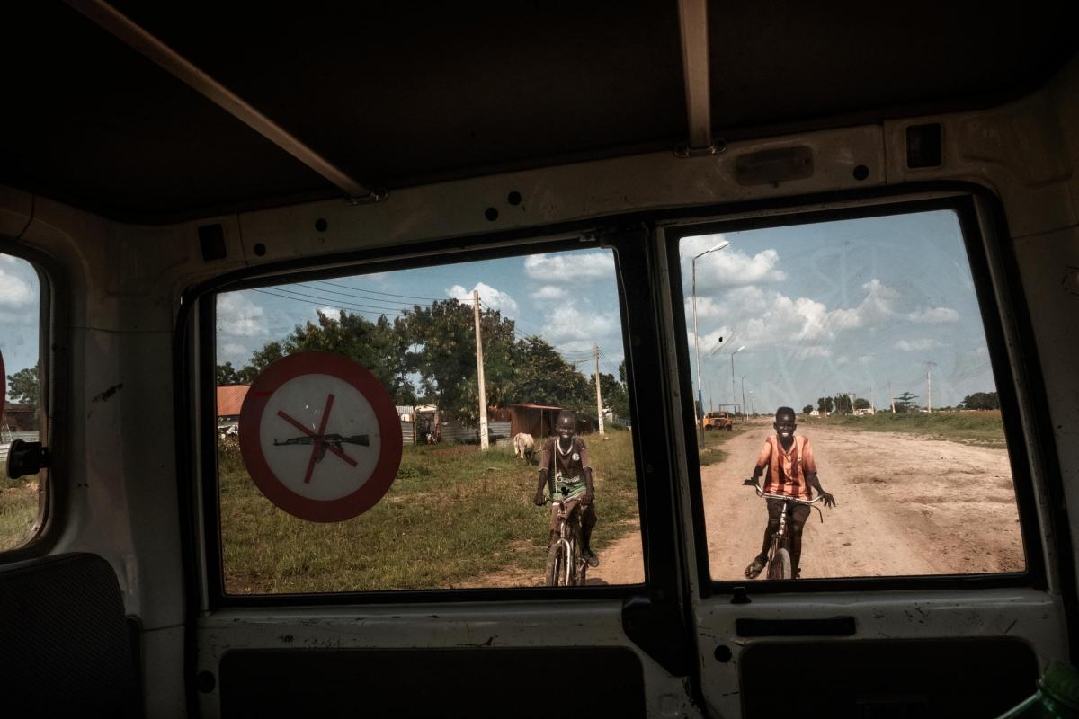 Deux enfants font du vélo derrière un véhicule MSF. La ville de Bentiu, autrefois un important centre&nbsp;administratif, politique et économique, est aujourd'hui en ruine.
 © Peter Bauza