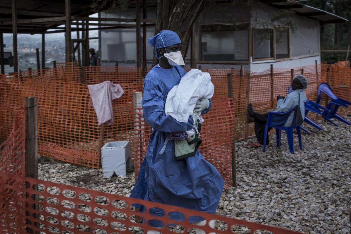 Un ancien patient Ebola aujourd'hui guéri est en train de transporter un nourrisson de 4 jours possiblement atteint par la maladie. Une fois guéris les patients Ebola sont immunisés contre la maladie et ont la possibilité de travailler à l'intérieur des zones à risque des centres de traitement. Butembo. Novembre 2018. République démocratique du Congo.
 © John Wessels