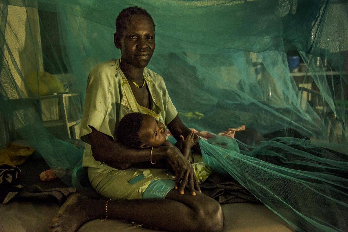 La nuit tombe sur le service pédiatrique de l'hôpital d’Old Fangak. Les moustiquaires ont été étendues autour des lits pour protéger des moustiques et du paludisme. Une patiente berce son enfant. 2017. Soudan du Sud.&nbsp;
 © Frederic NOY/COSMOS