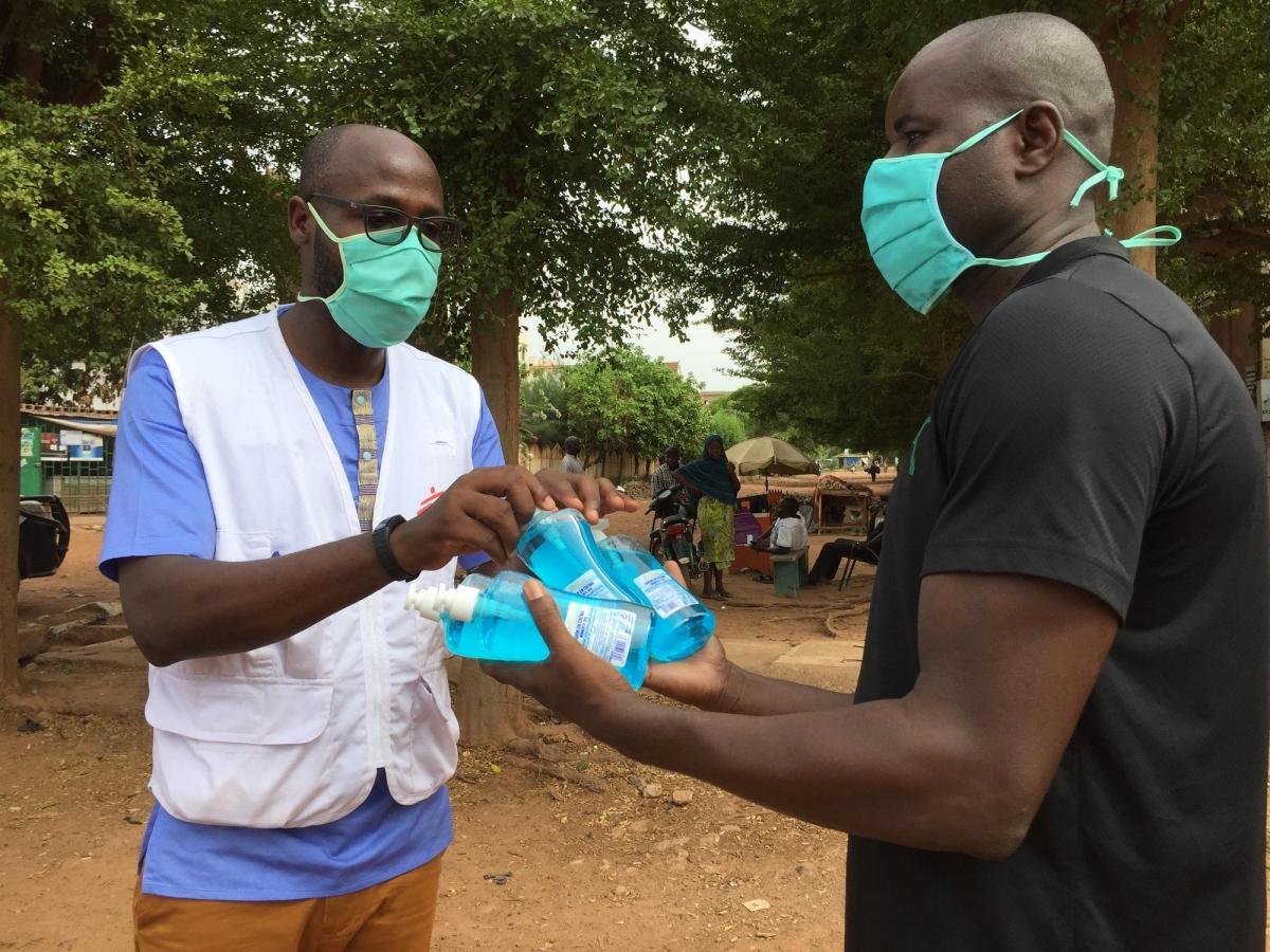 Kangni Cly, agent MSF, remet des savons liquides à un habitant pour les disposer à côté du kit de lavage de mains.
 © Lamine Keita/MSF