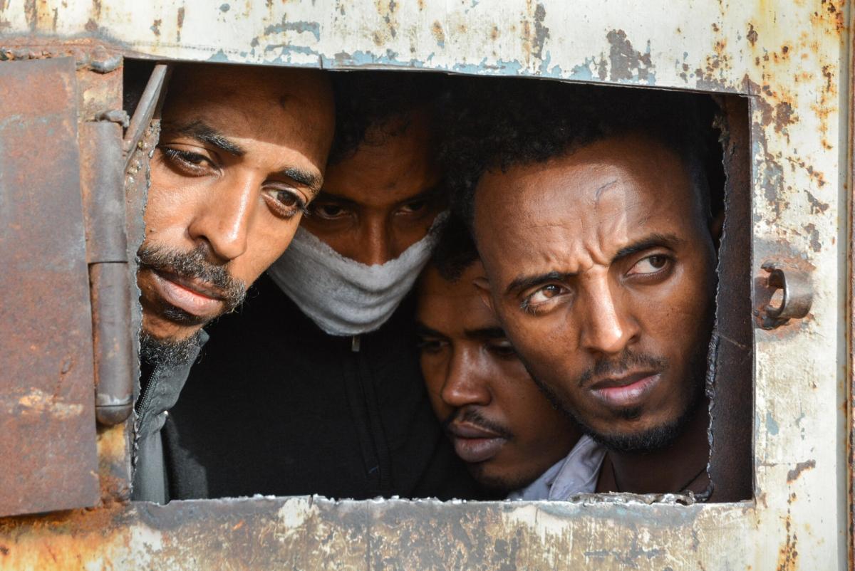 Réfugiés dans le centre de détention de Dhar al-Jebel, à la porte de l'entrepôt principal où 700 d'entre eux étaient détenus. Depuis 2016, MSF travaille, entre autres, dans des centres de détention où les migrants sont détenus arbitrairement et indéfiniment, fournissant aux détenus des soins de santé de base et un soutien psychosocial. Libye. 2019.
© Jérôme Tubiana/MSF
