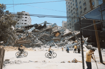 Des jeunes Gazaouis font du vélo devant un bâtiment détruit dans les bombardements sur la bande de Gaza. Mai 2021, Gaza.