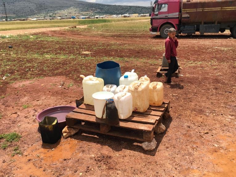 Un jeune Syrien passe à côté des bidons utilisés pour recueillir l'eau dans un camp de personnes déplacées à Idlib en Syrie.&nbsp;
 © Mohammed Homidan/MSF