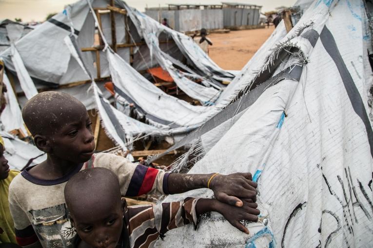 Deux enfants se tiennent devant un abri détruit dans le camp de transit de Pulka.&nbsp;
 © Igor G. Barbero/MSF