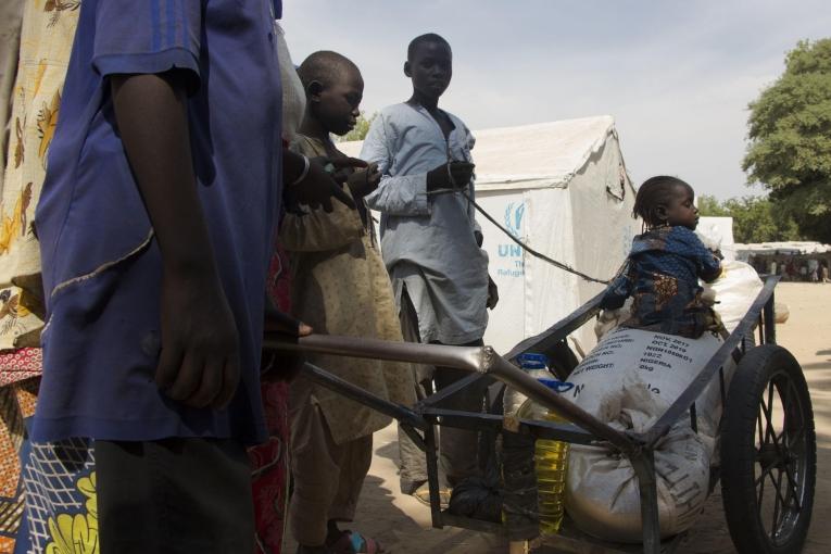 Une petite fille est assisse sur les six mois de rations de nourriture de sa famille après une distribution dans le camp pour personnes déplacées de Bama. Nigeria. 2018.
 © Natacha Buhler/MSF