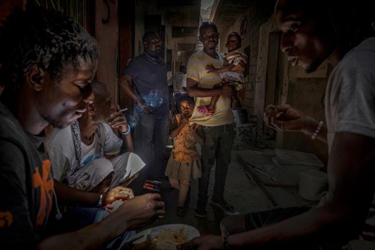 Un groupe de migrants et de réfugiés mangent tandis qu'un père et son fils de deux ans les regardent. Libye. Août 2021.
 © Ricardo Garcia Vilanova