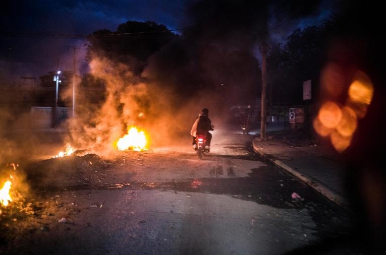 Un homme circule à moto dans les rues en feu de Port-au-Prince, en proie aux combats menés par les gangs qui tentent de prendre le contrôle de la capitale haïtienne.

En novembre 2024, à la suite de graves menaces proférées à l’encontre de son personnel par des membres des forces de police haïtiennes, MSF a temporairement suspendu ses activités à Port-au-Prince. La prise en charge des patients a pu reprendre partiellement en décembre.&nbsp;&nbsp;

Mars 2024. Haïti. ©&nbsp;Corentin Fohlen/Divergence
