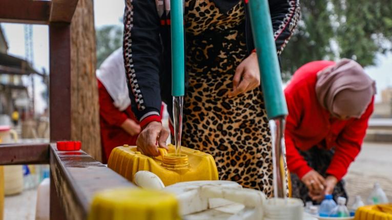 Des robinets d'eau publique alimentés par un grand réservoir, devant lesquels des femmes remplissent des bidons d'eau dans le quartier de Ghweiran, à Hassaké, dans le nord-est de la Syrie.
 © Gihad Darwish/MSF