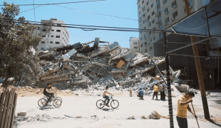 Des jeunes Gazaouis font du vélo devant un bâtiment détruit dans les bombardements sur la bande de Gaza. Mai 2021, Gaza.