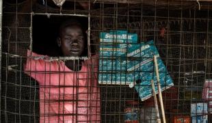 Un jeune garçon gère un petit magasin de denrées alimentaires de base dans l’un des marchés du camp. Soudan du Sud. 2017.