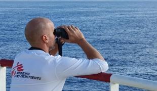 Jay Berger, coordinateur de projet MSF, regarde à travers des jumelles un canot pneumatique en détresse alors que les équipes de MSF et de SOS Méditerranée se préparent à secourir les 104 personnes à bord.