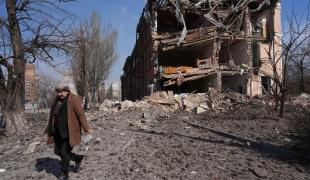 Une femme passe devant un bâtiment endommagé par un bombardement à Marioupol, Ukraine. 13 mars 2022.