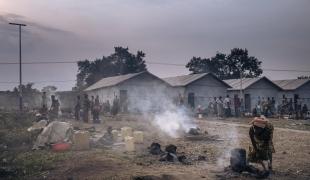 Une femme prépare de la nourriture à l'aube devant les abris communautaires du site informel pour personnes déplacées du stade de Rugabo.