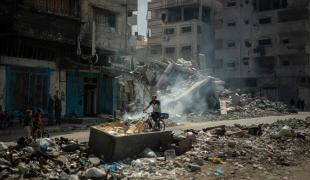 Dans le camp de réfugié d'Al Shate, dans la ville de Gaza, un homme se déplace en bicyclette au milieu des immeubles détruits. Septembre 2024.