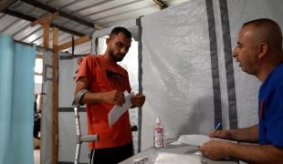 Un membre du personnel de MSF consulte le dossier médical de Saad Hussein, contraint de vivre avec un fixateur externe depuis qu'il a été blessé en 2025 lors d'une distribution alimentaire organisée par la Fondation humanitaire de Gaza. 