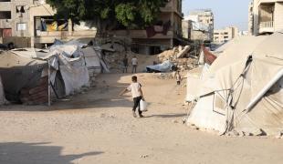 Un petit garçon peine sous le poids d'un jerrican d'eau qu'il doit ramener jusqu'à la tente où vit sa famille déplacée, territoires palestiniens occupés, octobre 2025.