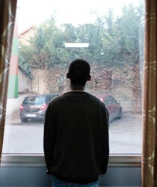 Un jeune bénéficiaire du projet MSF Passerelle regarde par la fenêtre depuis l’hôtel. 2018. France.