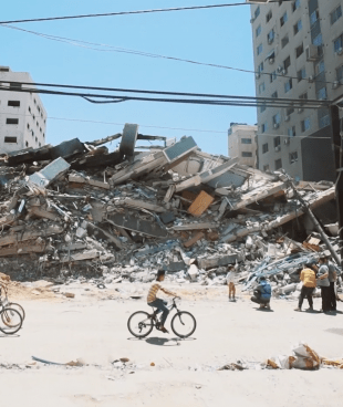 Des jeunes Gazaouis font du vélo devant un bâtiment détruit dans les bombardements sur la bande de Gaza. Mai 2021, Gaza.