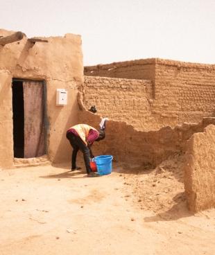 Un migrant lave son linge devant la maison qu'il loue avec d'autres dans un ghetto d'Agadez. Celles et ceux qui passent par Agadez luttent pour trouver un emploi afin de gagner de l'argent pour avoir un endroit où dormir, de la nourriture, et pour continuer leur voyage.