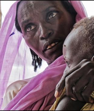 Une femme tient son enfant dans les bras, en attendant de recevoir des soins médicaux dans un centre de santé MSF au Nord-Darfour. Soudan. 2014