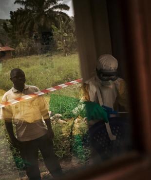 Un laborantin observe le travail des équipes MSF et regarde notamment comment ils vont réussir à désinfecter le microscope et les outils de son laboratoire. Certains éléments comme le papier seront brûlés car impossible à décontaminer. République démocratique du Congo. 2018.