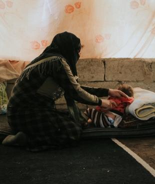 Une femme prend soin de sa fille dans la tente d'un camp de personnes déplacées. Nord-ouest de la Syrie. 2022.
