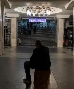 Un homme est assis sur un banc dans le métro. Autour de lui, des wagons où vivent désormais des personnes qui fuit les bombardements à Kharkiv. 11 avril 2022. Ukraine.