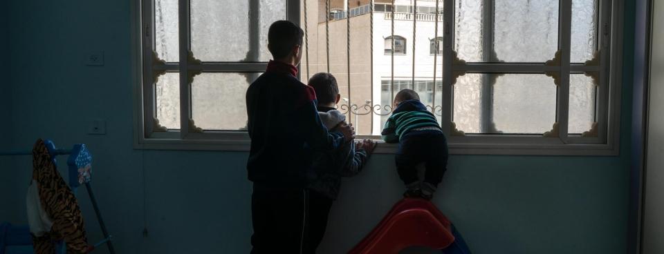 Hussam et ses cousins regardent un soldat israélien par la fenêtre de leur maison de Huwara. Avril 2023. Cisjordanie.