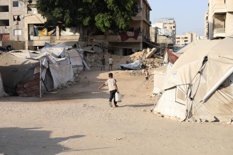 Un petit garçon peine sous le poids d'un jerrican d'eau qu'il doit ramener jusqu'à la tente où vit sa famille déplacée, territoires palestiniens occupés, octobre 2025.