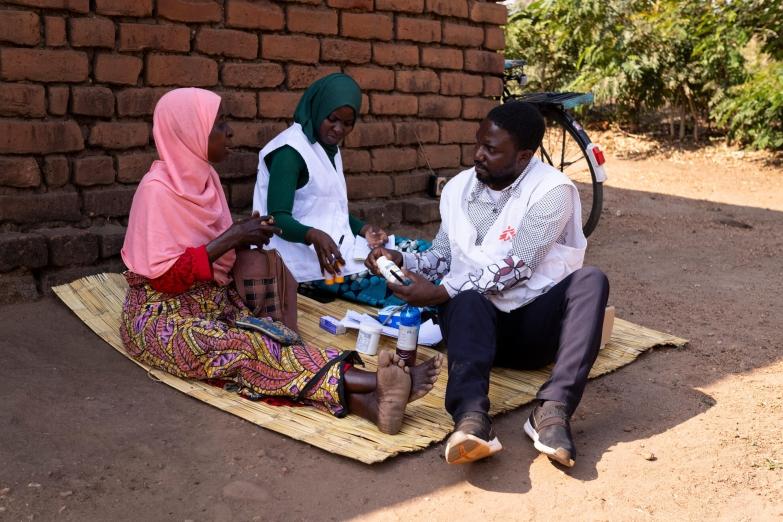 Une patiente dans son village avec deux membres de l'équipe de MSF qui lui apportent une aide médicale face à son cancer.